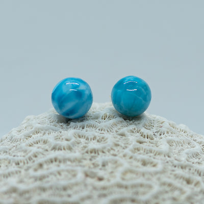 Deux perles de larimar bleue intense posées sur un coquillage. Ces pierres naturelles sont extraites en République Dominicaine et taillées à la main par un artisan à Saint-Domingue.