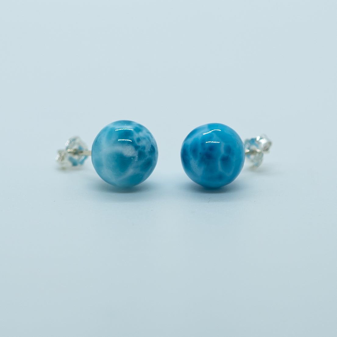 Vue de face de deux perles en pierre naturelle de couleur bleu, le larimar, montées en boucles d'oreilles avec tige et fermoir en argent 925.