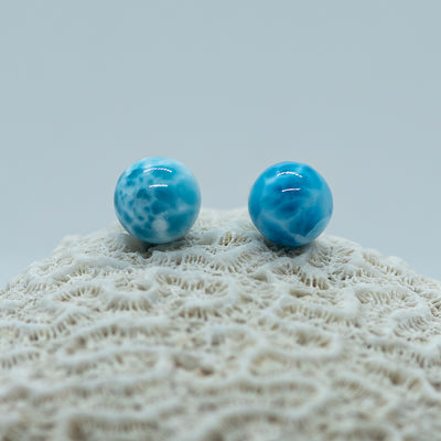 Coquillage blanc sur lequel sont posées deux perles bleues qui semblent être su Larimar de République Dominicaine. Plusieurs nuances de bleue sont visible sur les perles.