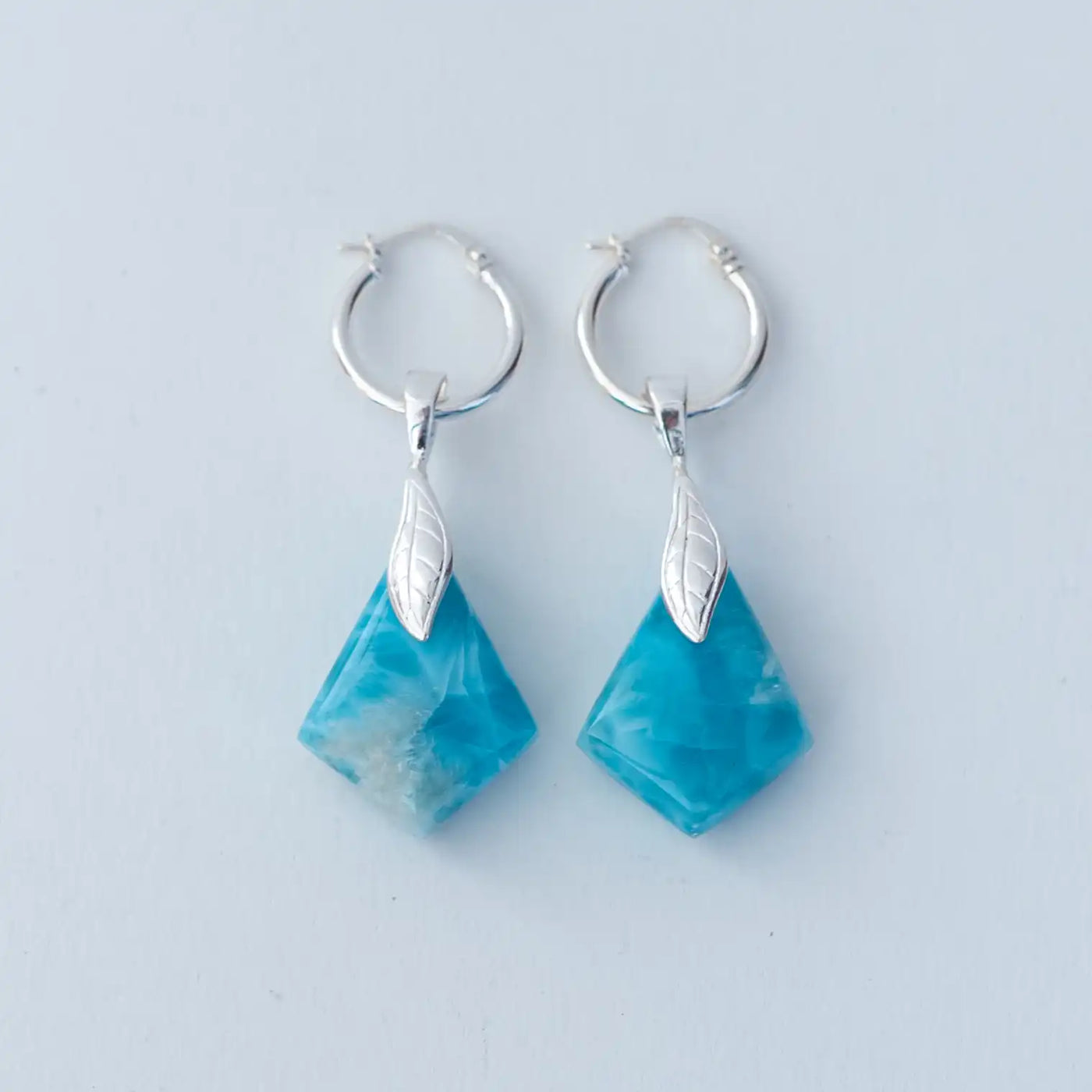 Pierres naturelles de larimar taillées en losanges, de couleur bleu, montées sur des petites créoles en argent 925. Boucles d'oreilles en pierres naturelles.