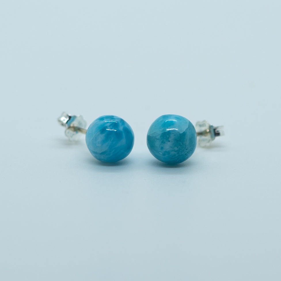 Vue de face de deux perles rondes bleues, taillées dans la pierre naturelle de larimar, montées en boucles d'oreilles en argent 925.