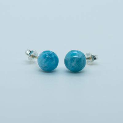 Vue de face de deux perles rondes bleues, taillées dans la pierre naturelle de larimar, montées en boucles d'oreilles en argent 925.