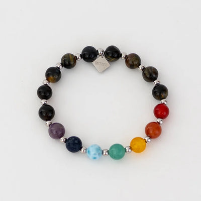 Photo d'un bracelet en fil elastique fait en oeil du tigre, une pierre de protection. Sept perles de couleur différents représentent les sept chakras, dont une perle de larimar. Breloque orparima sur le bracelet.