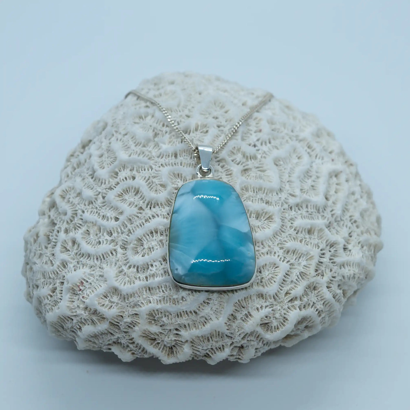 Collier posé sur un coquillage blanc sur fond gris clair. Bijou en Larimar serti en argent 925 en République Dominicaine.