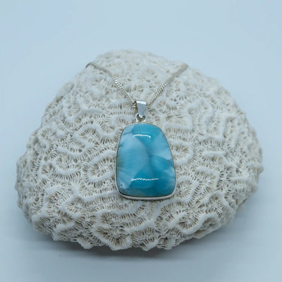 Collier posé sur un coquillage blanc sur fond gris clair. Bijou en Larimar serti en argent 925 en République Dominicaine.